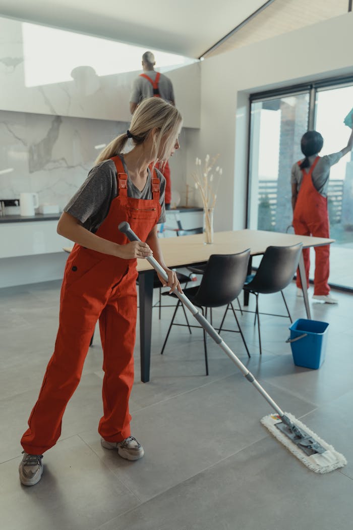 hero-img-02 Cleaning team in red overalls mopping and sanitizing a modern home interior.